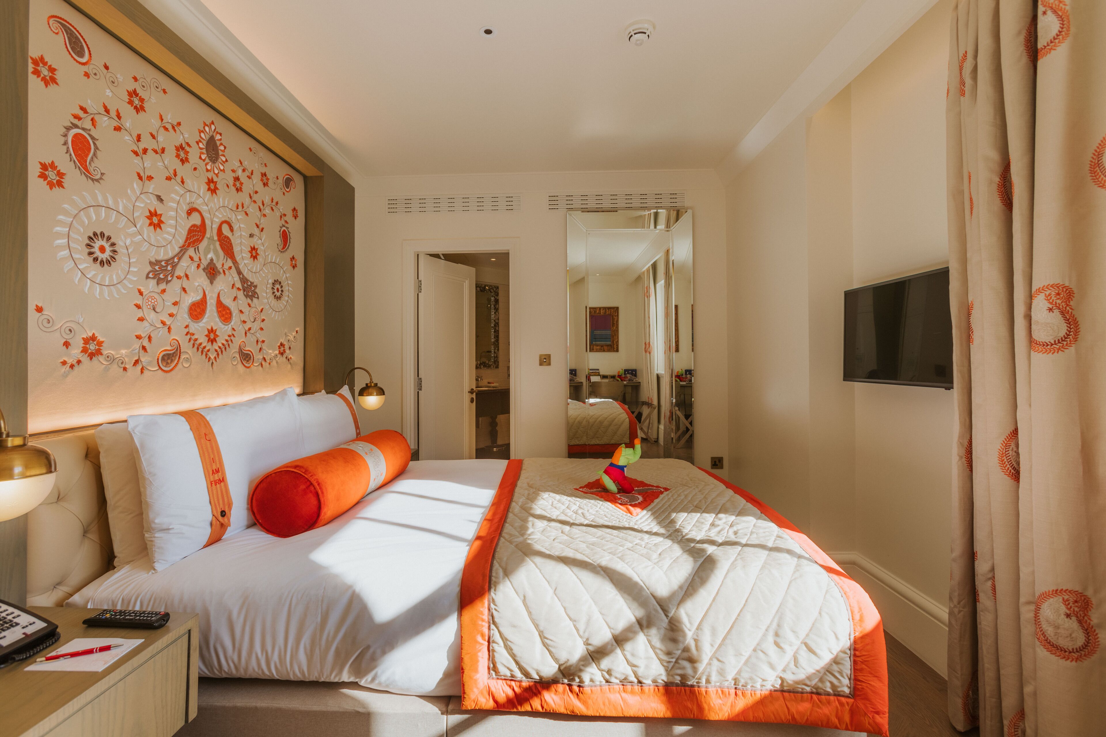 Een hotelkamer met een groot bed, een nachtkastje met lamp, een aan de muur bevestigde televisie en een spiegel boven het bed.