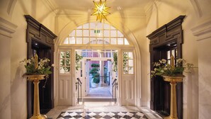 A grand entrance with a checkered floor, two ornate gold columns, and a star-shaped ceiling light. - The Lalit London (London)