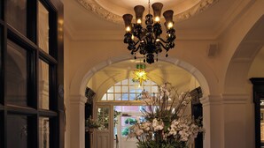 A lobby with a black and white checkered floor, a large ornate chandelier, and a floral arrangement in the center. - The Lalit London (London)