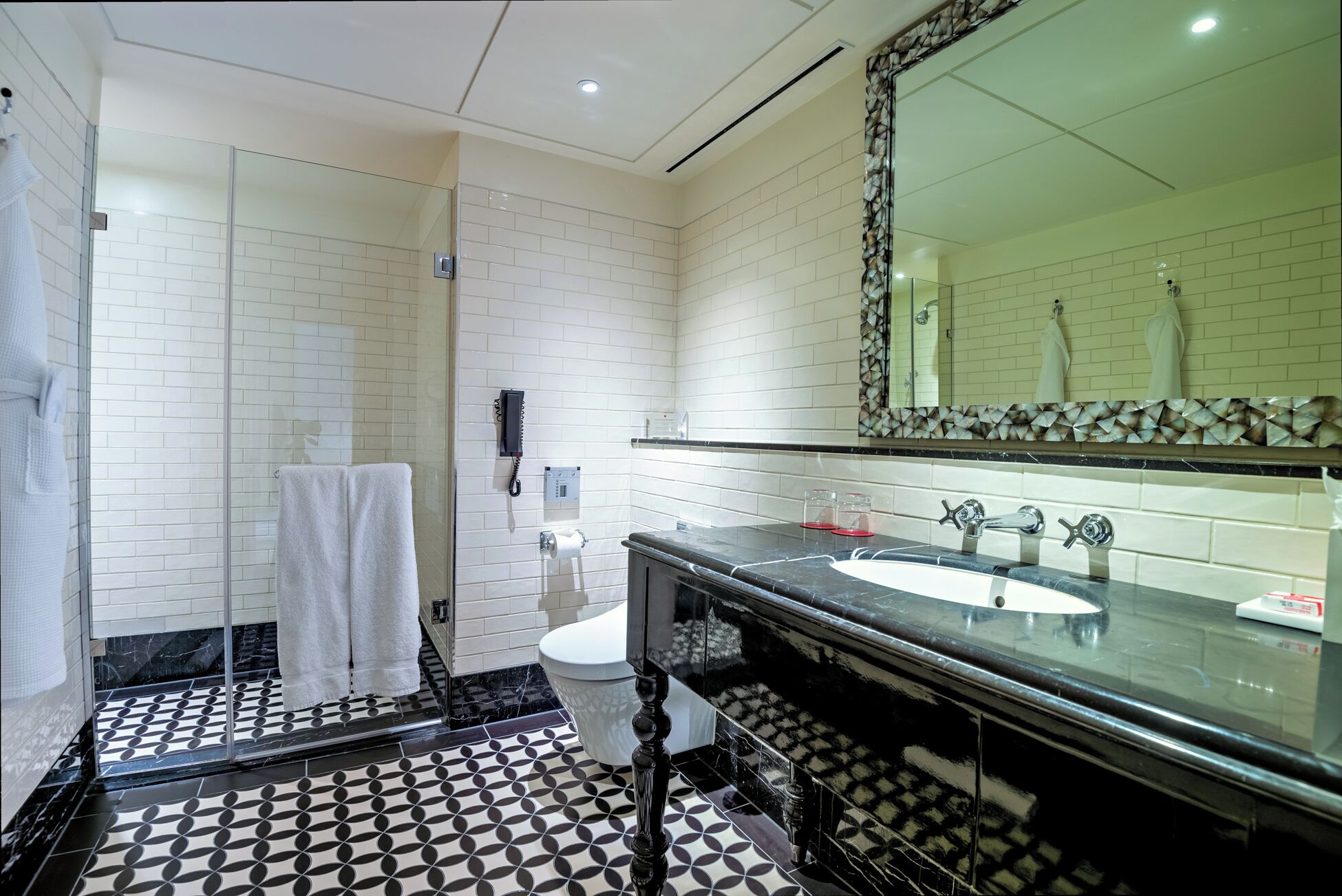 A modern bathroom with a glass shower enclosure, a white toilet, a large mirror with a decorative frame, and a black marble countertop with a white sink.