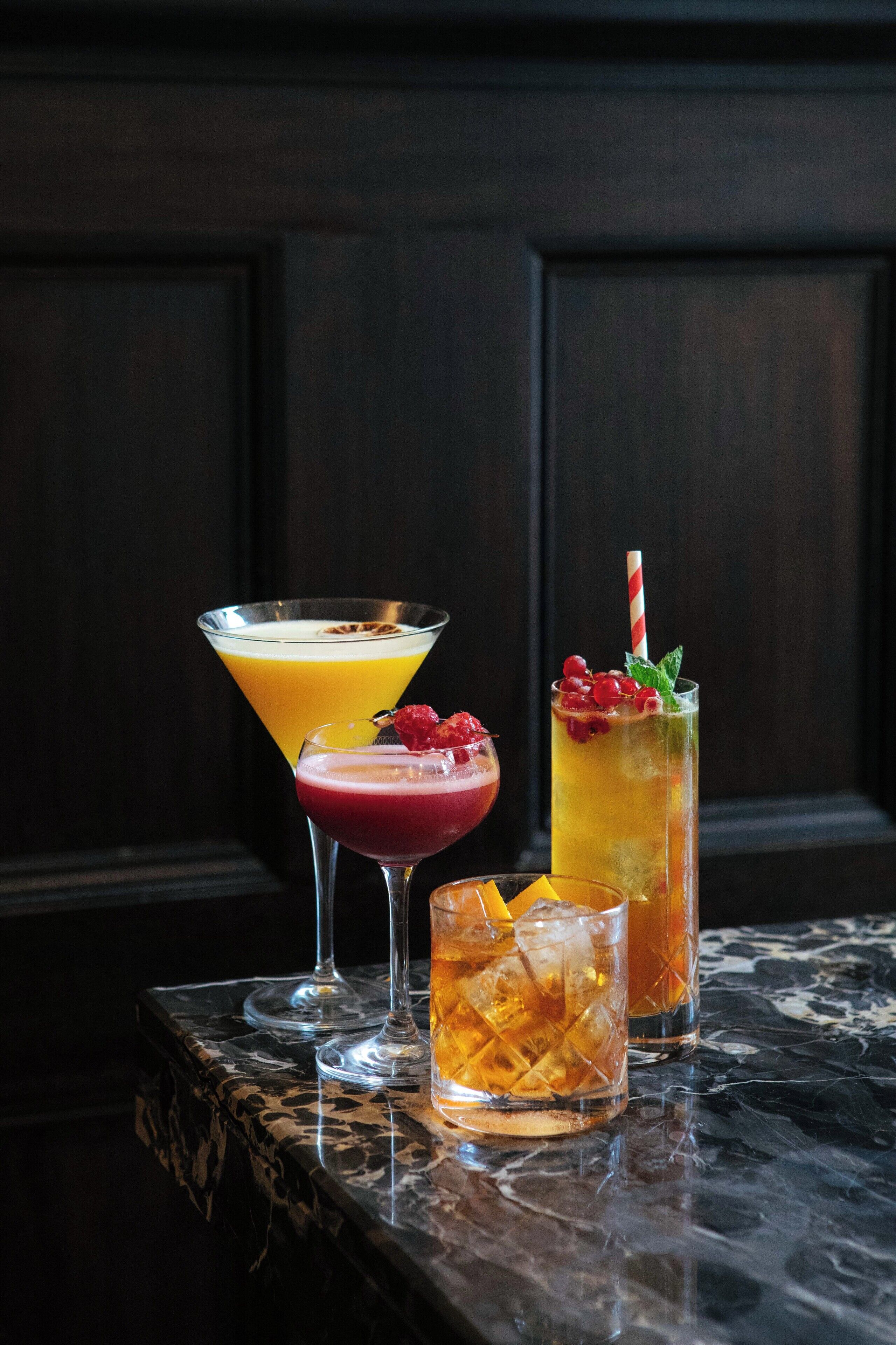 Tres bebidas sobre una mesa de mármol con fondo de madera oscura.