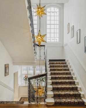 Stunning staircase with a patterned carpet and elegant lighting, leading to a cozy landing with a potted plant.