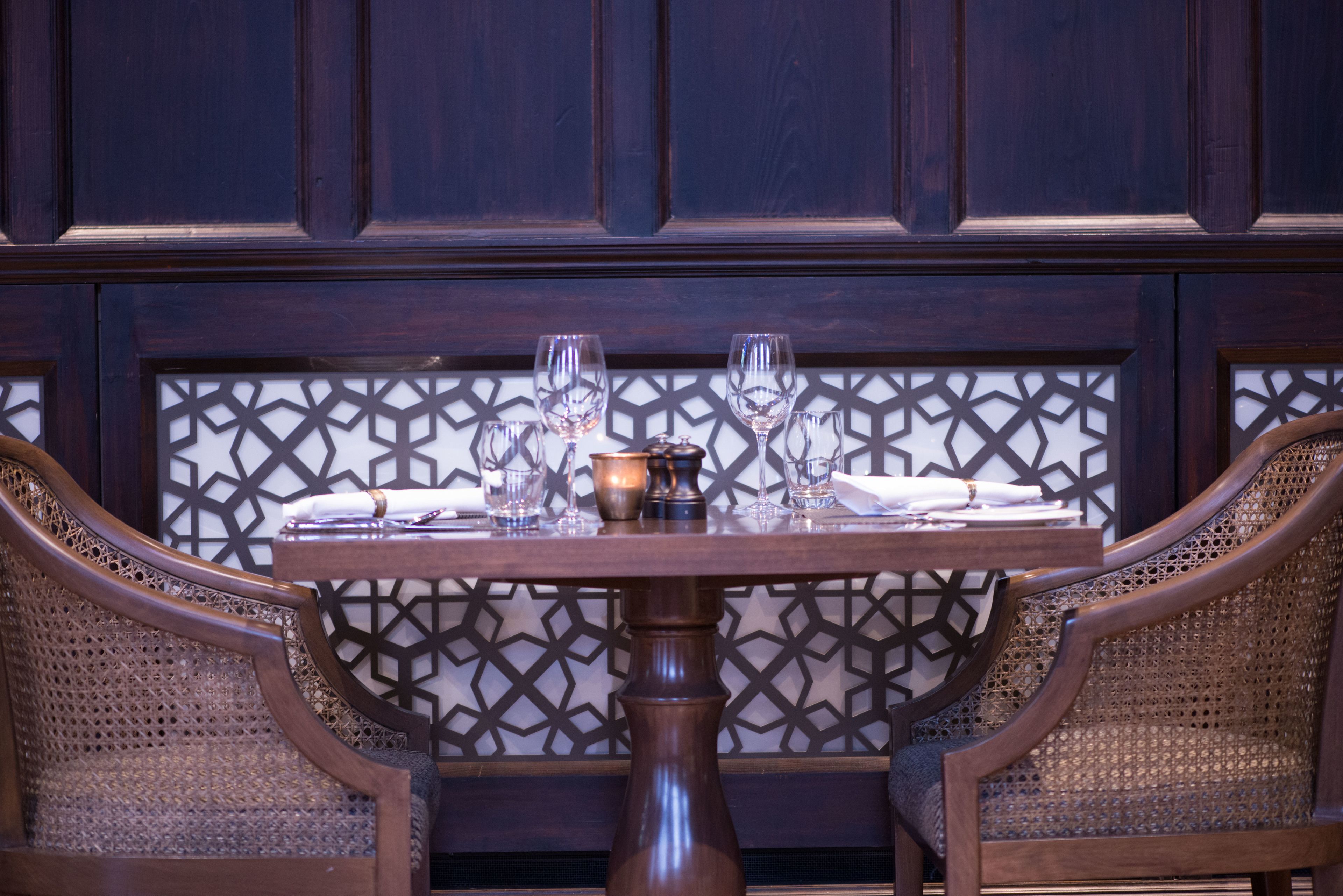 A dining table with four wine glasses and a bowl, set against a geometric patterned wall.