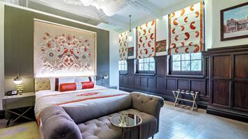 A hotel room with a large bed, a seating area, and a view of the city through large windows.