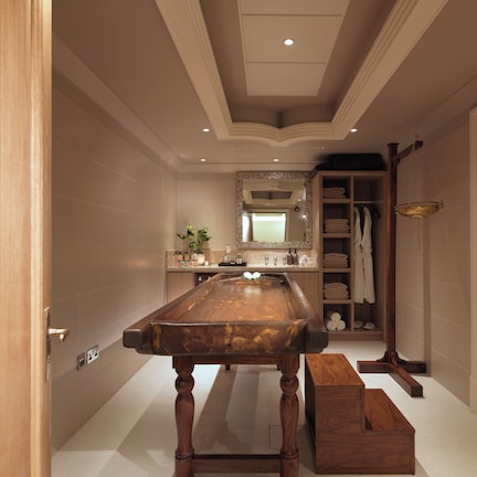 A spacious bathroom with a wooden bathtub, a large mirror, and a built-in shelf with towels.