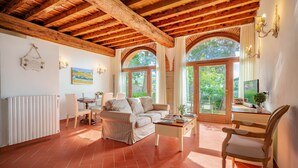 A spacious living room with a high wooden ceiling, a fireplace, and large windows offering a view of the outdoors. - Casabella Residenza d'Epoca (Vaglia)