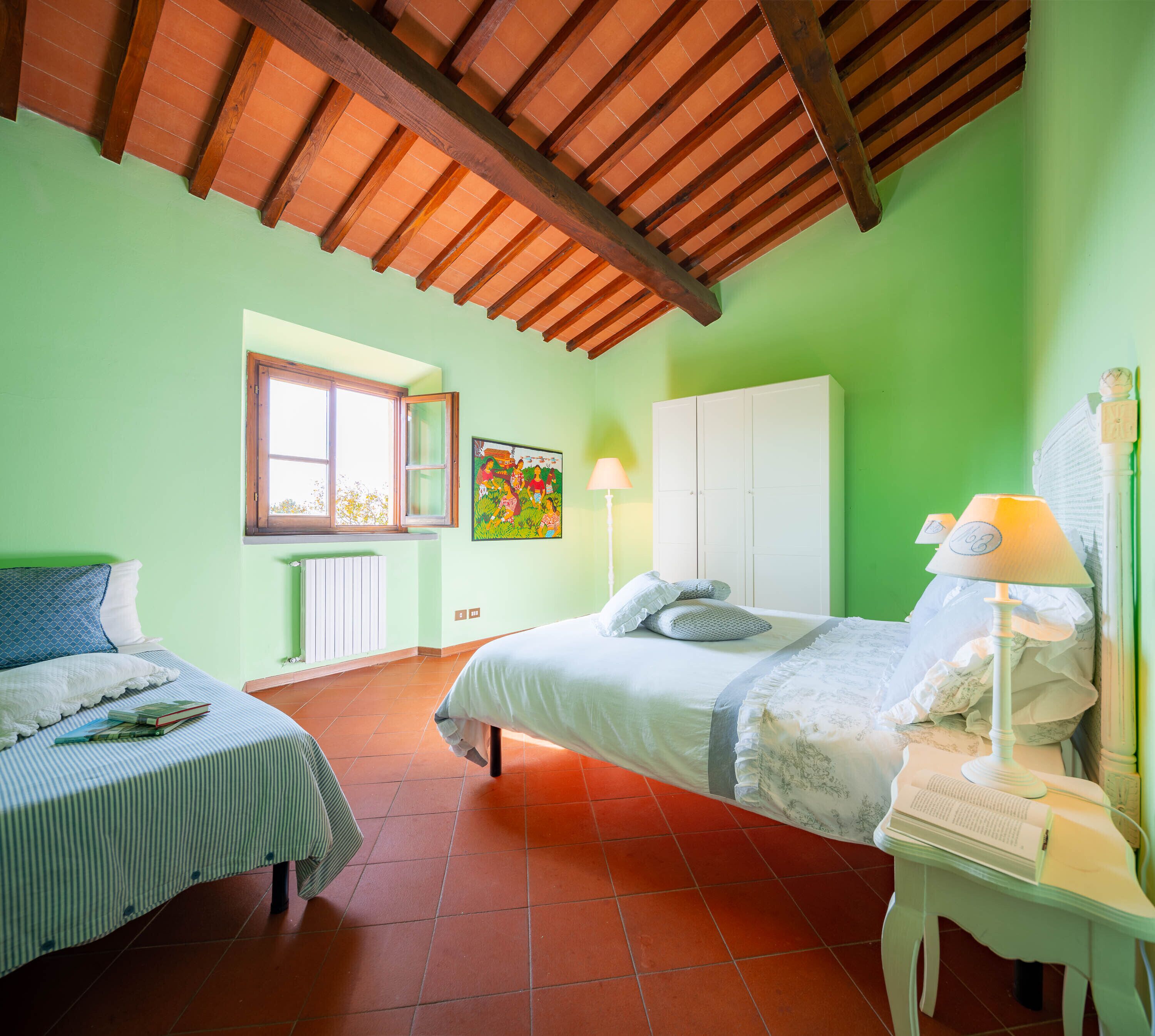A room with two beds, a window, a radiator, a lamp, and a cabinet.