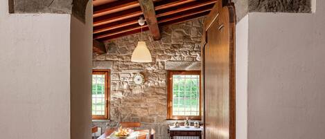 Una habitación rústica con paredes de piedra, una mesa y sillas de madera, una lámpara colgante y una ventana con vistas a la vegetación.