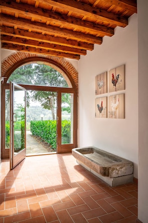 An open doorway leading to a garden, a rustic wooden ceiling, and a wall with framed rooster illustrations.