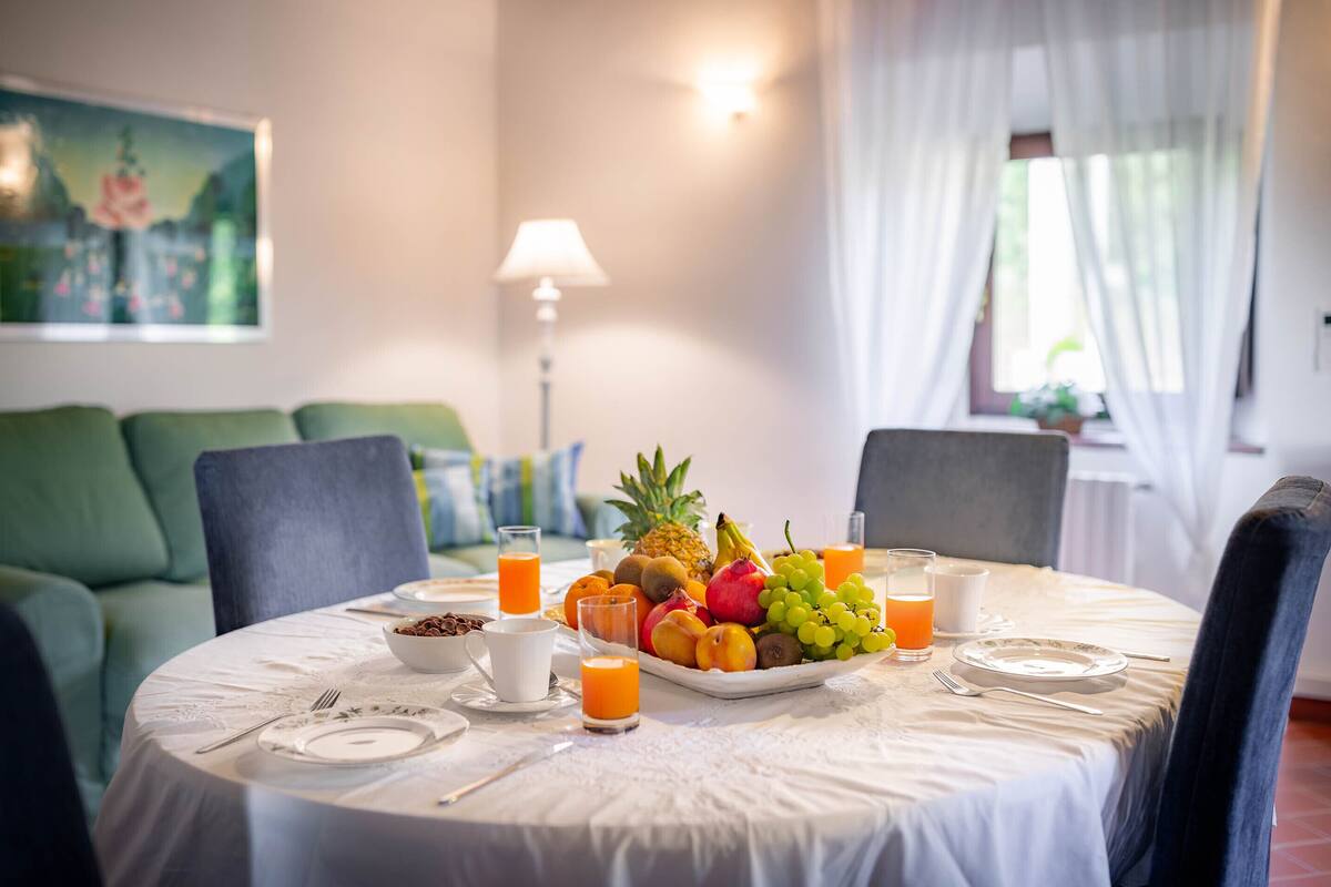 A dining table set with fruits and juice, a green sofa, and a lamp in a room with a painting on the wall.