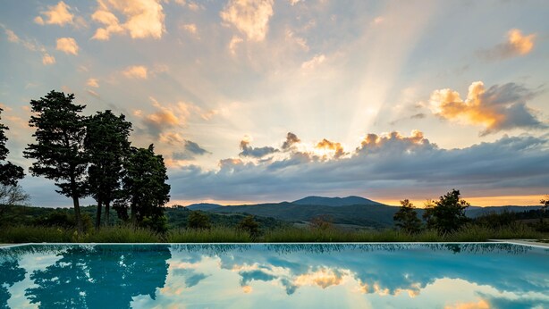 A clear swimming pool reflecting the sky and trees, surrounded by a natural landscape with hills in the distance. - Casabella Residenza d'Epoca (Vaglia)