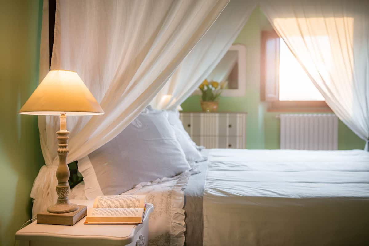 A neatly made bed with a white bedspread, a bedside table with a lamp, and a book.