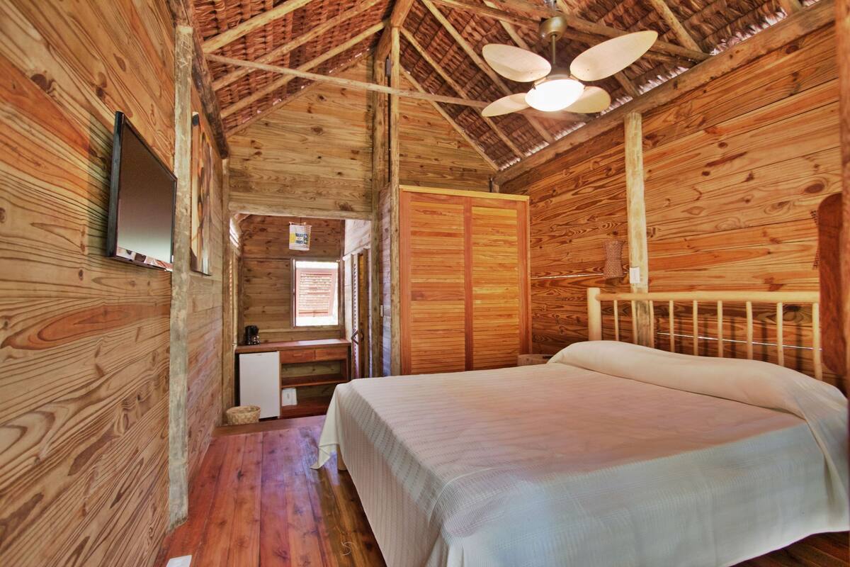 A wooden cabin room with a bed, a desk, and a wardrobe.