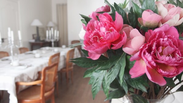 Un comedor con una mesa dispuesta para cuatro, sillas y un jarrón de flores rosas.
