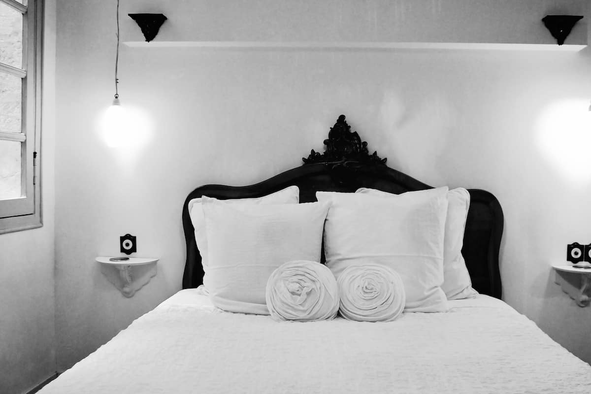 A neatly made bed with white linens, a dark headboard, and two bedside tables with decorative items.