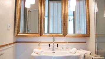 Un baño con un lavabo grande de color blanco, dos espejos con marcos dorados y una zona de ducha.