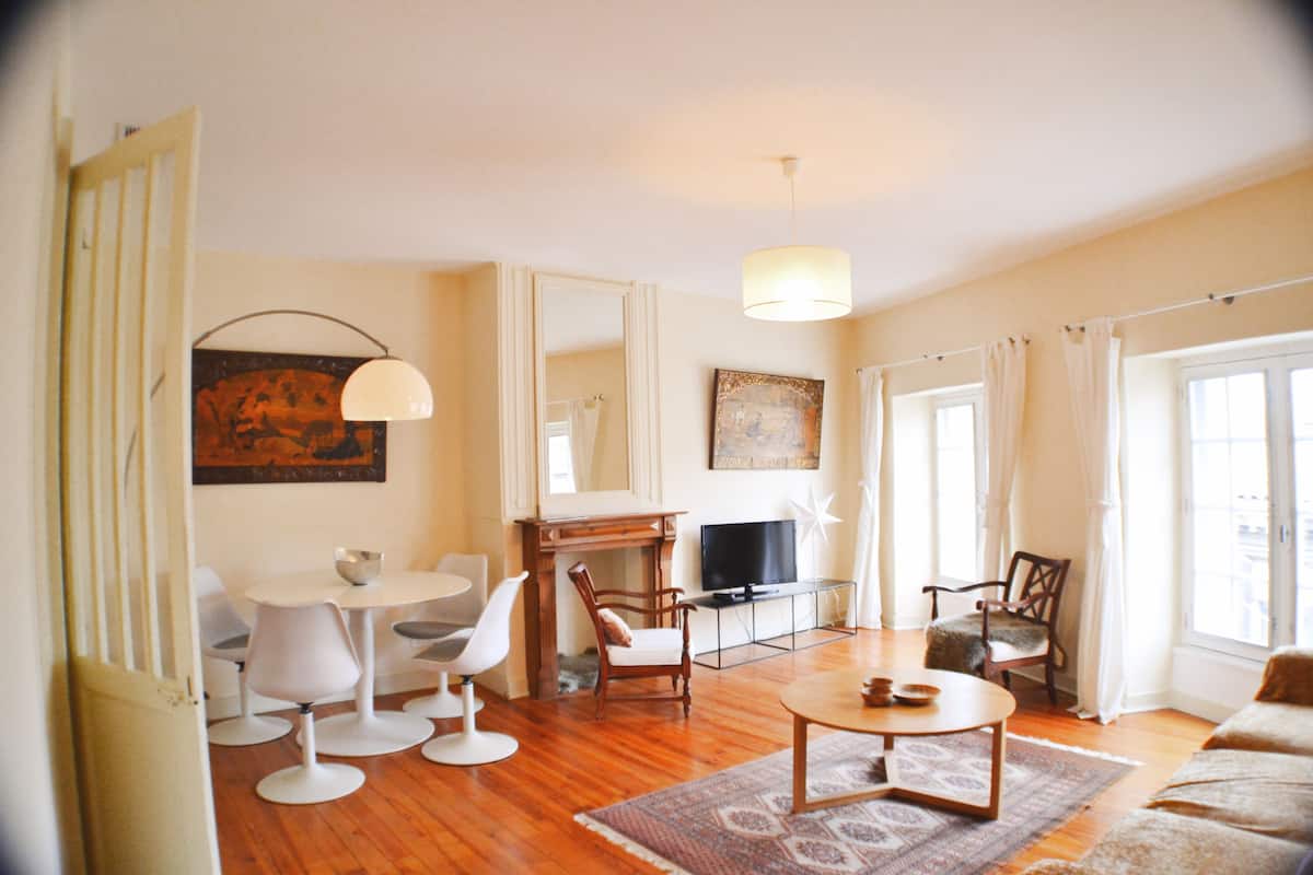 A living room with a round coffee table, a television, and a fireplace. There are two chairs and a sofa.