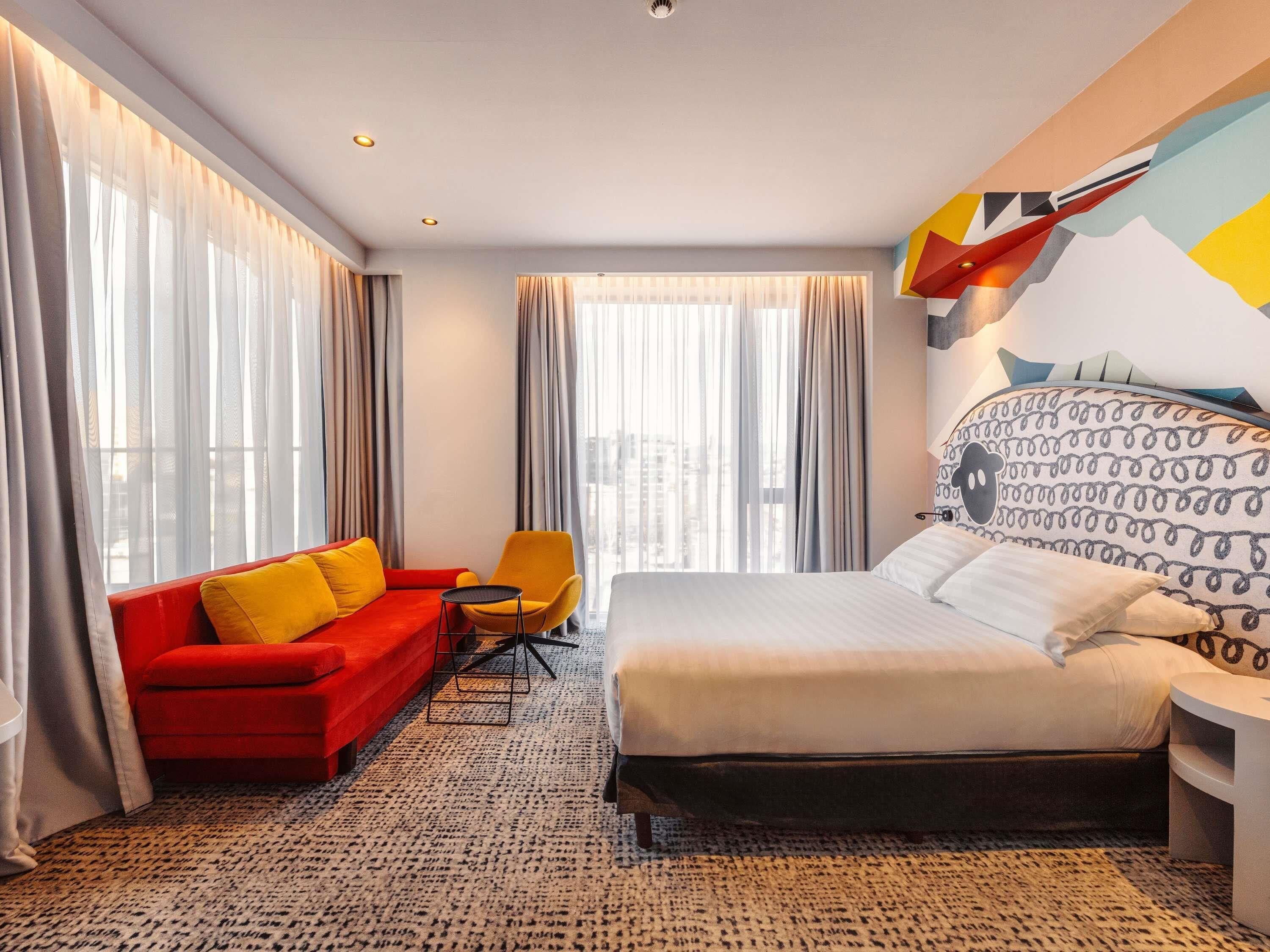 Een hotelkamer met een bed, een rode bank, een gele fauteuil en een klein tafeltje.