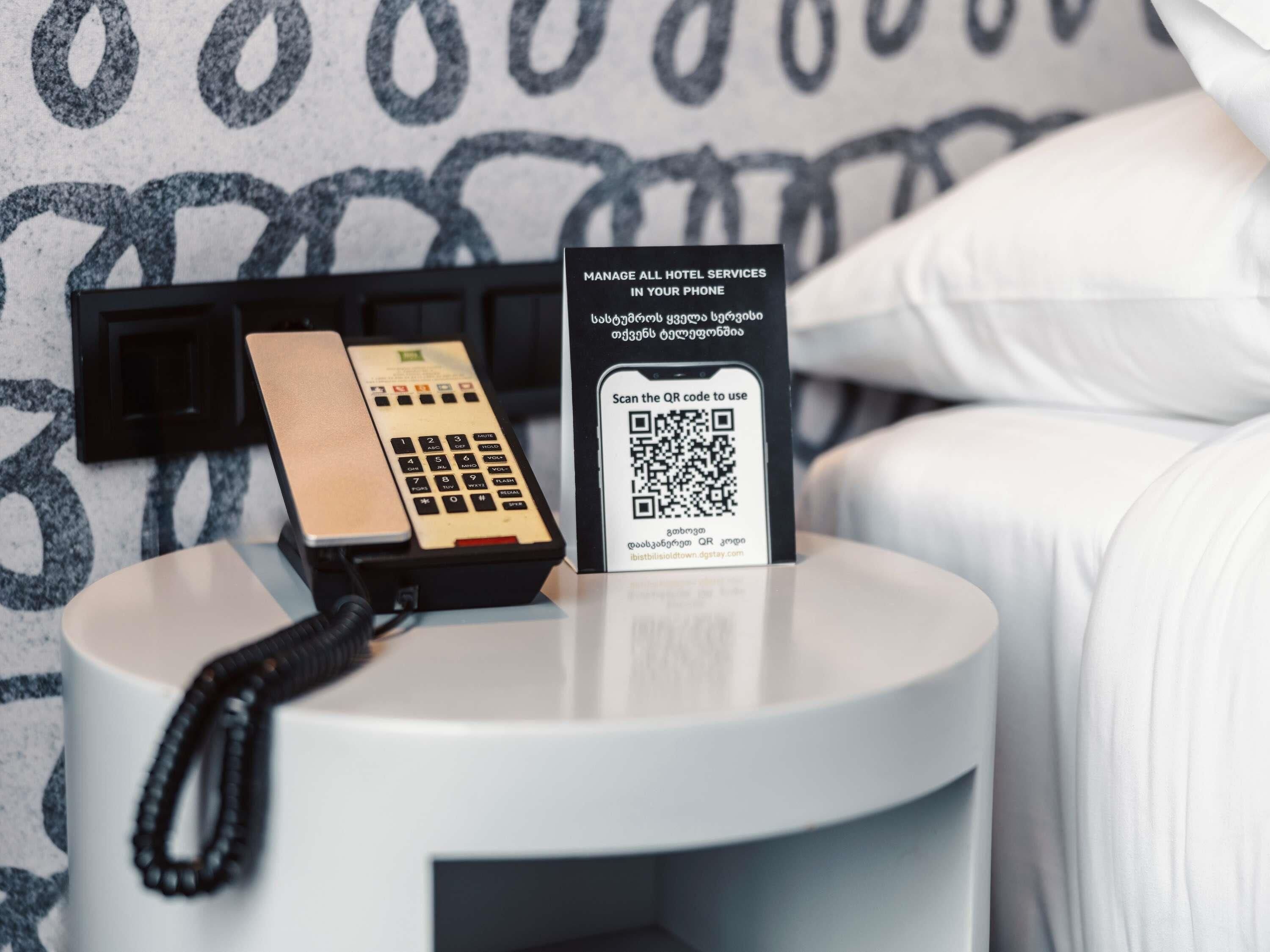 Een hotelkamer met een bedtelefoon, een QR-code voor dienstverlening van het hotel, en een zwarte telefoonkabel.