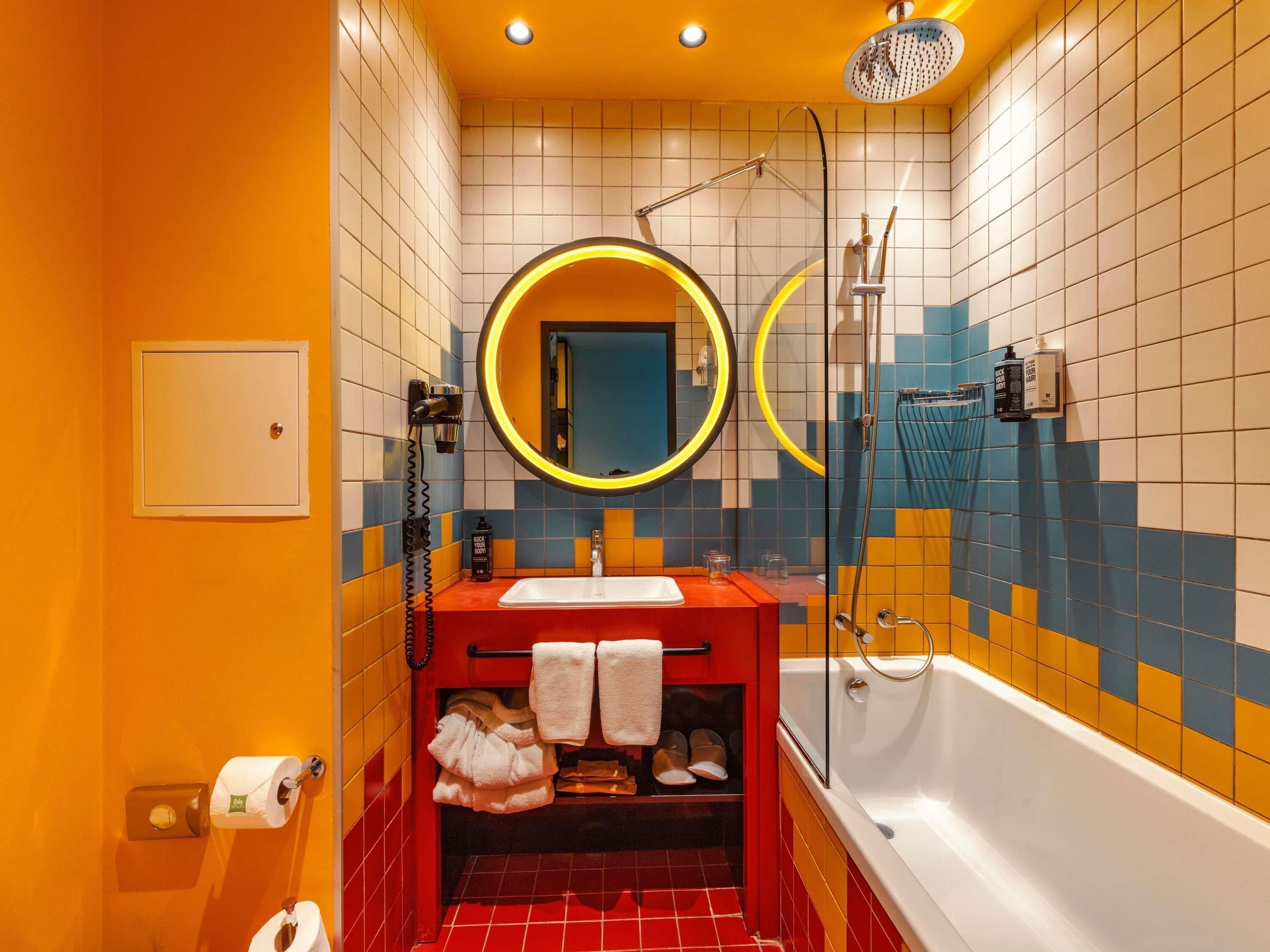 A bathroom with a red sink, a mirror with a yellow frame, a shower, and a toilet.