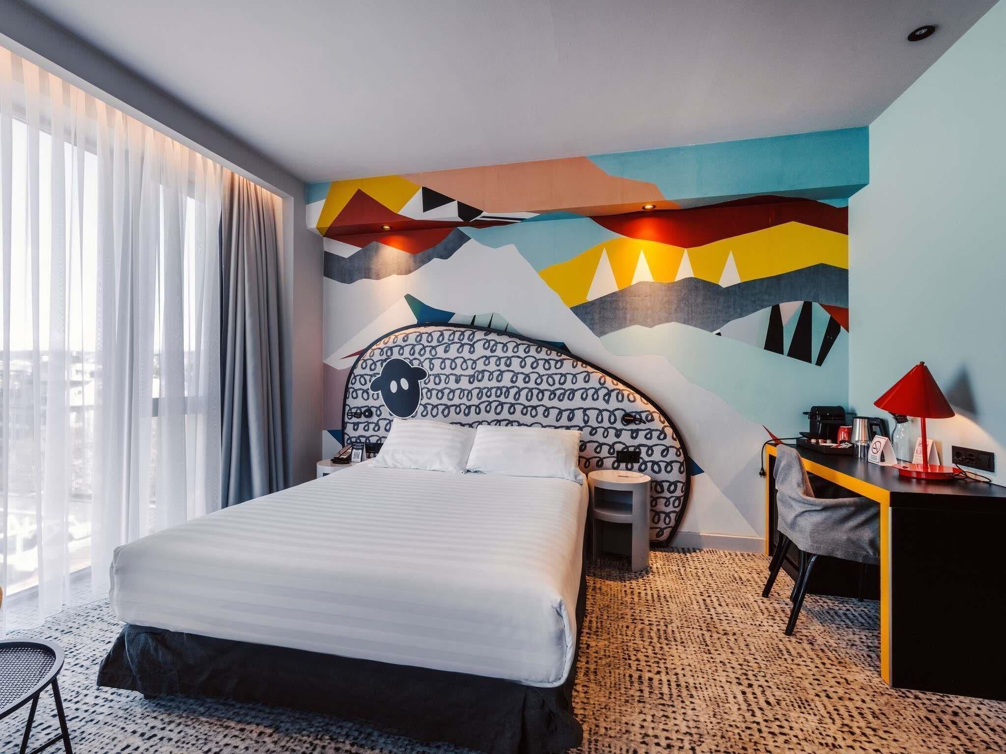 A modern hotel room with a large bed, a desk, and a chair.
