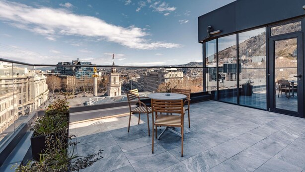 A rooftop terrace with a table and chairs, overlooking a cityscape with buildings and a mountain. - Ibis Styles Tbilisi Center (Tbilisi)
