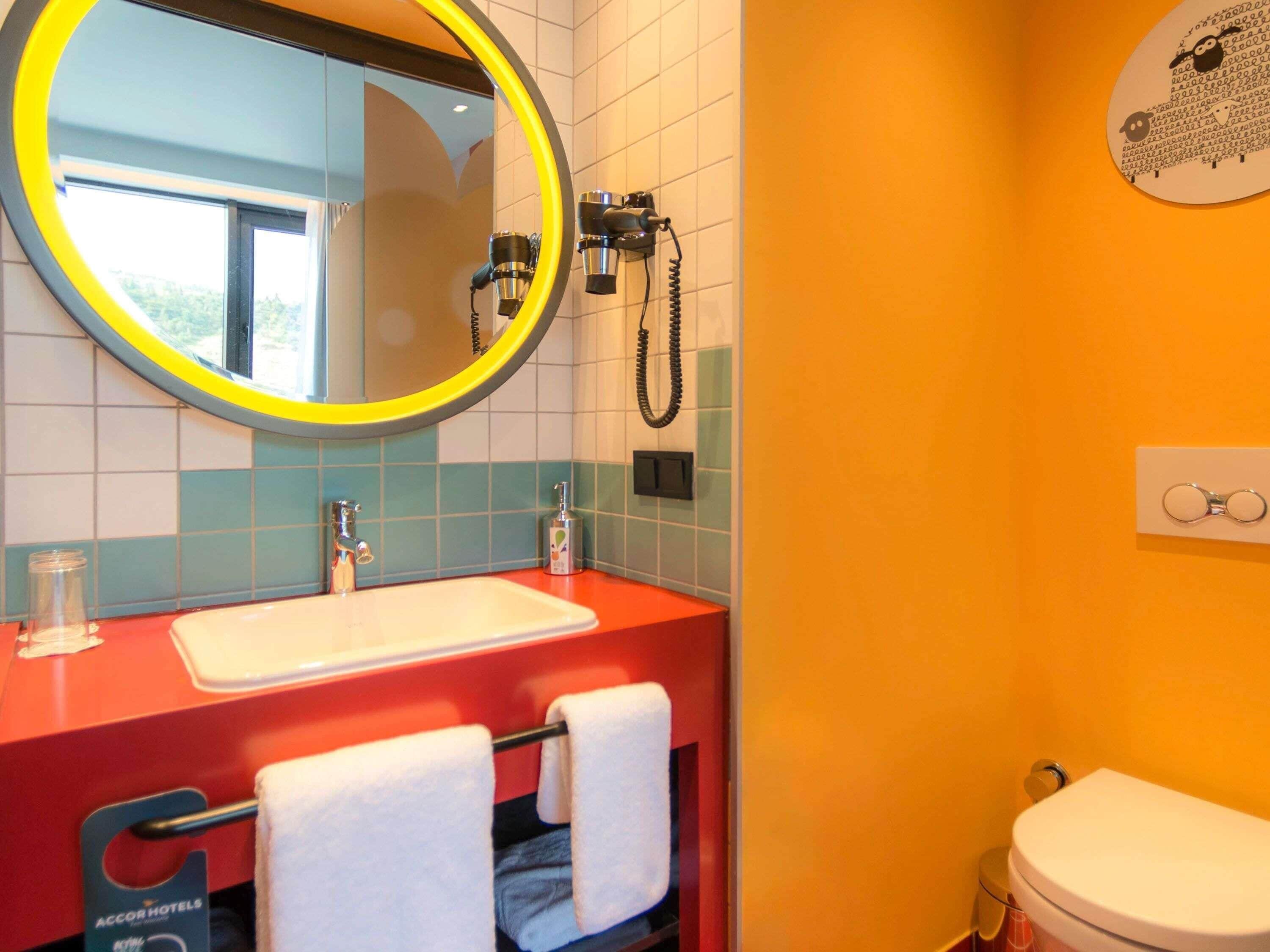 A bathroom with a round mirror, a sink, a toilet, and a towel rack.