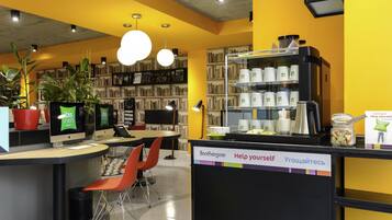 A hotel lobby with a coffee station, seating area, and a bookshelf filled with books.
