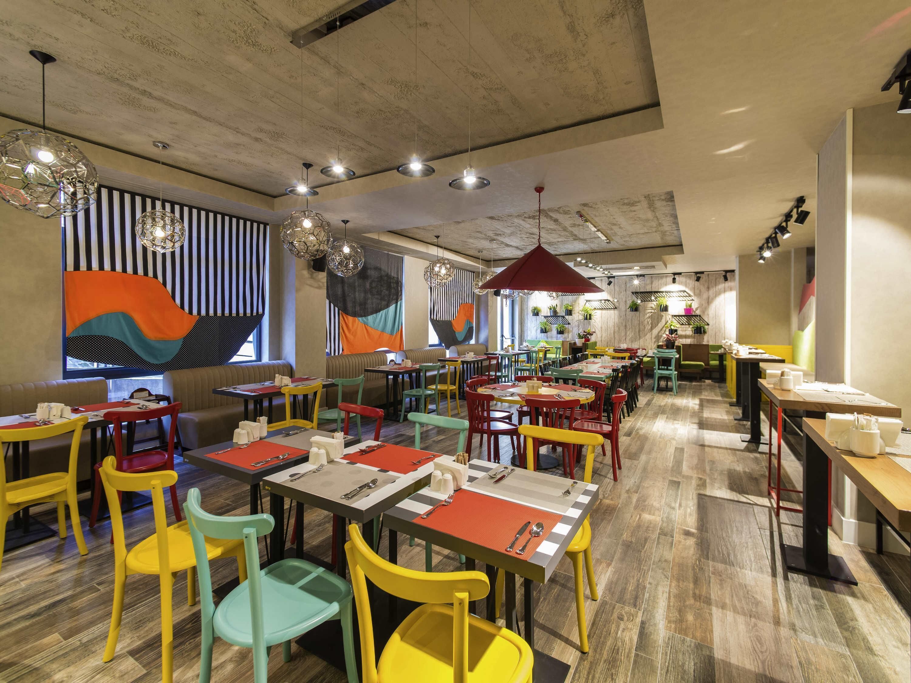 A restaurant with multiple tables and chairs, a concrete ceiling, and hanging pendant lights.