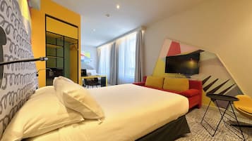 A hotel room with a large bed, a red sofa, a TV, and a desk with a chair.