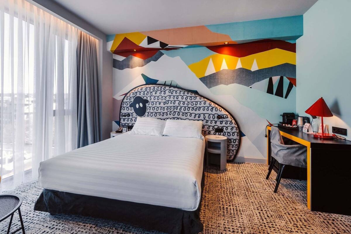 A modern hotel room with a large bed, a desk, and a chair.