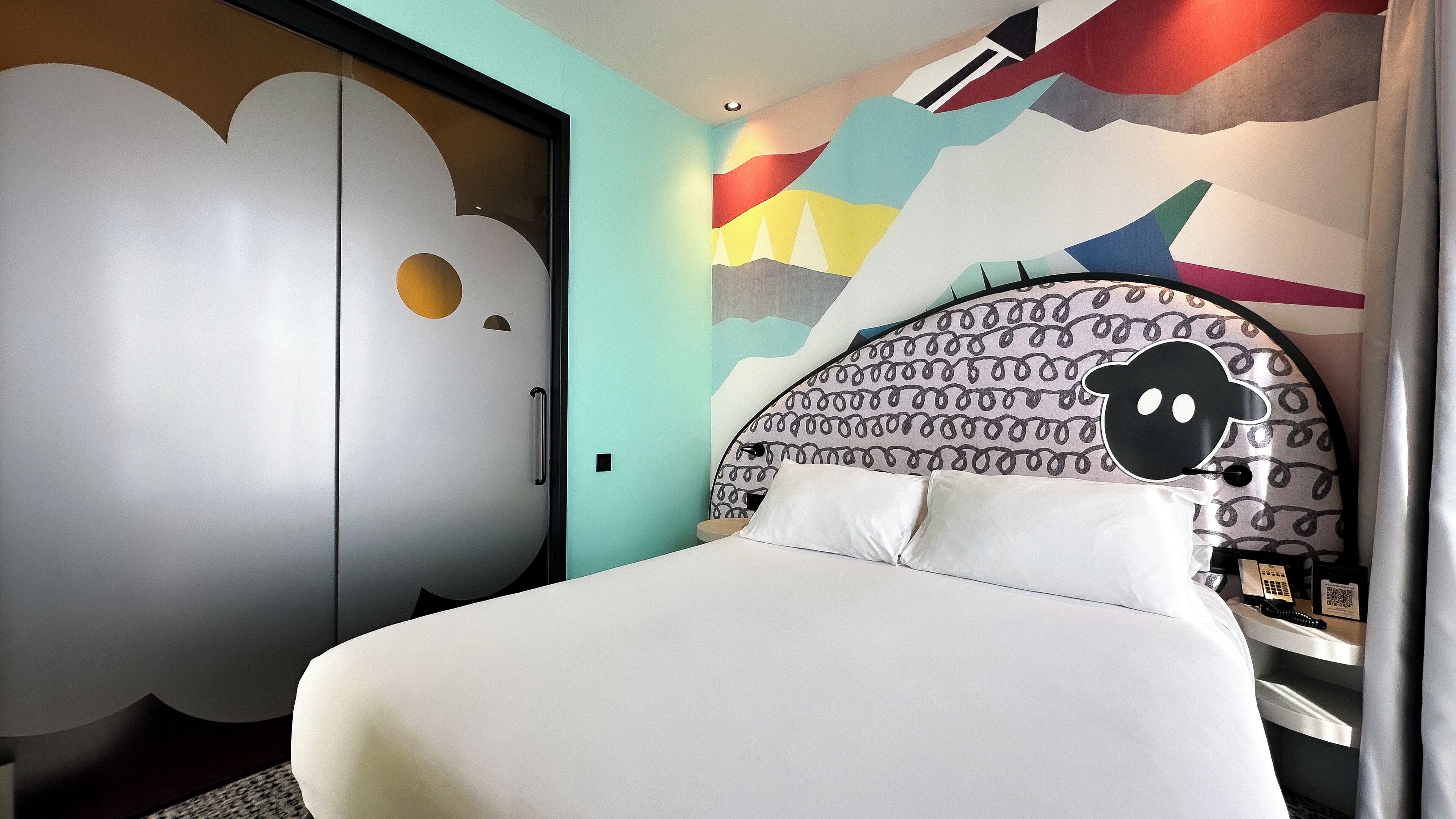 A modern bedroom with a bed, a wardrobe, and a wall with abstract art.
