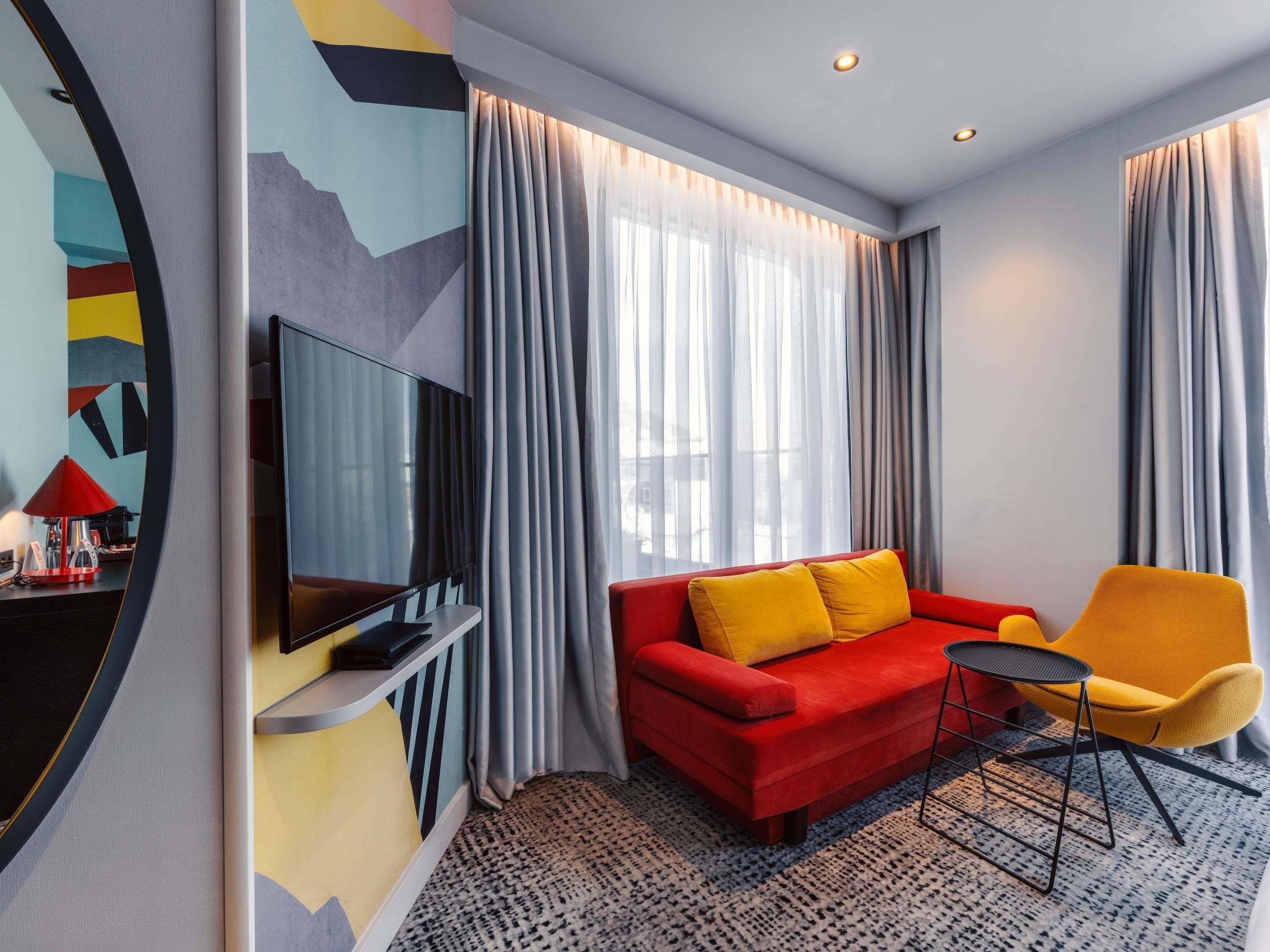 Una sala de estar moderna con un sofá rojo, un sillón amarillo y un televisor de pantalla plana sobre un mueble.