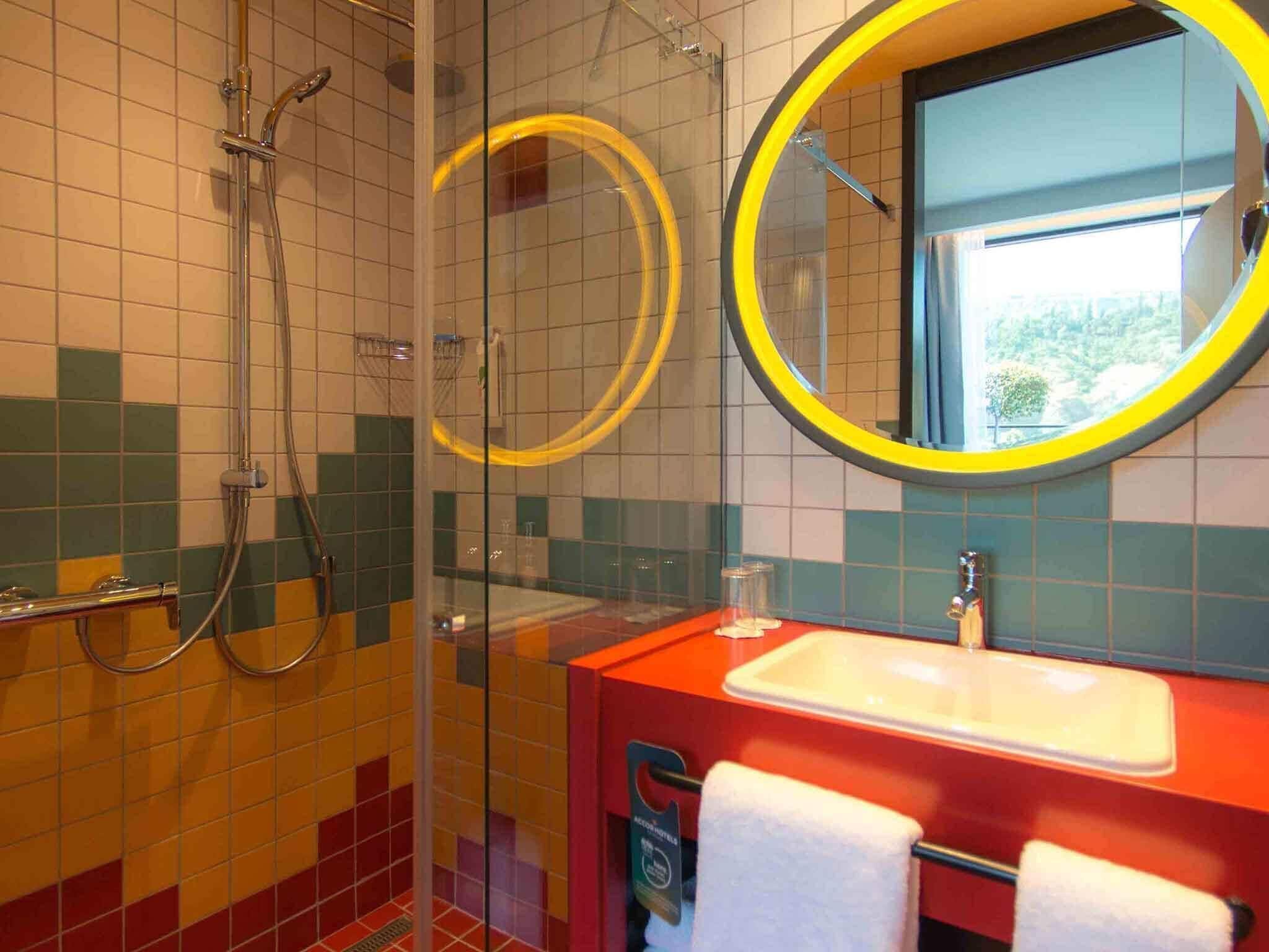 A bathroom with a glass-enclosed shower, a red sink, and a mirror with a yellow frame.