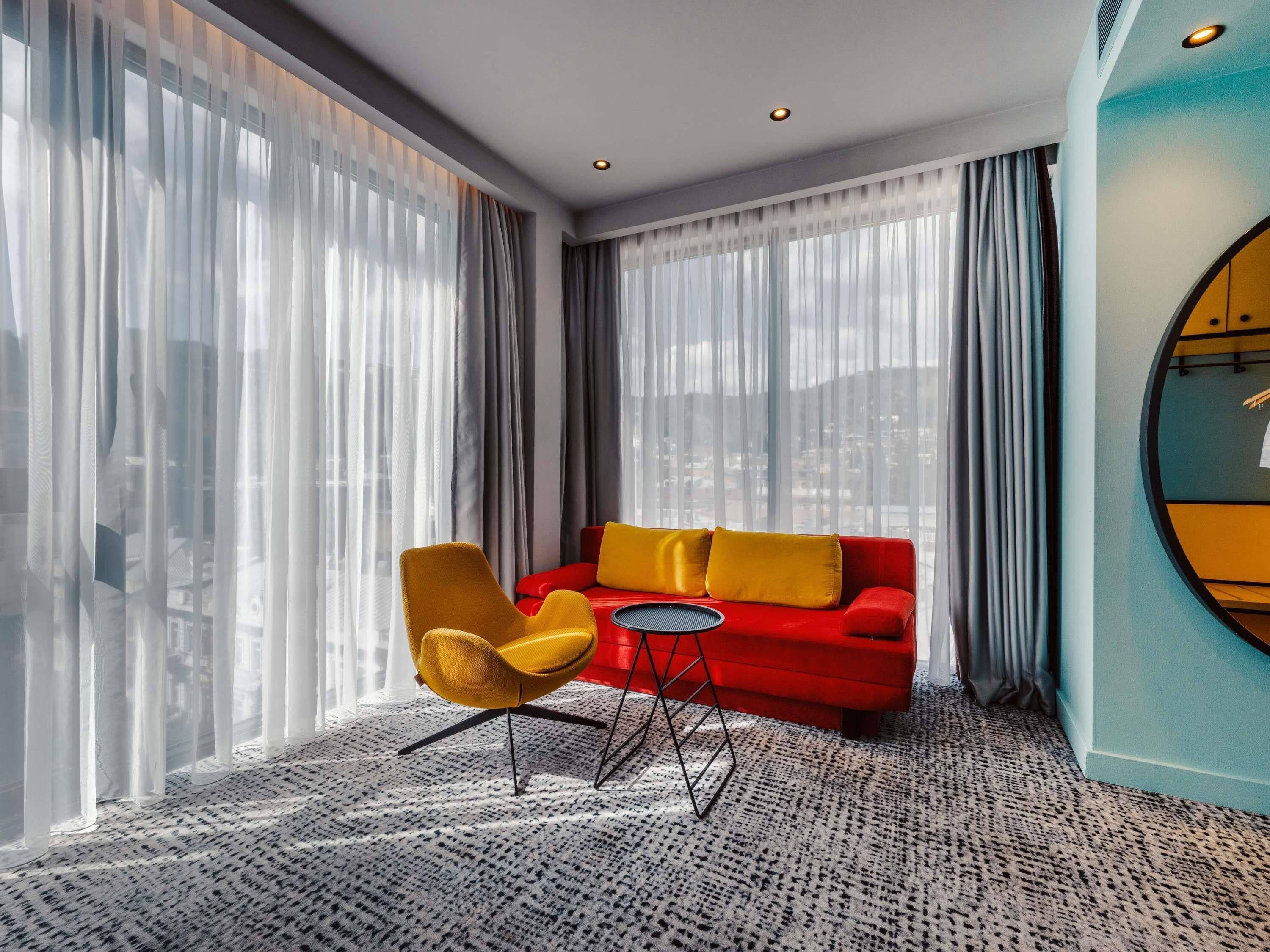 Et moderne hotelværelse med en rød sofa, en gul lænestol og et rundt bord.