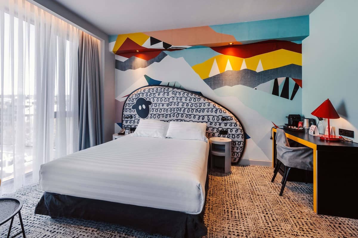 Et moderne hotelværelse med en stor seng, et skrivebord, en stol og udsigt over byen.