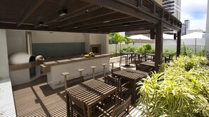 Eine Außenpatio-Terrasse mit Holztischen und -stühlen, eine Bar mit Theke und Hockern sowie Kübelpflanzen.