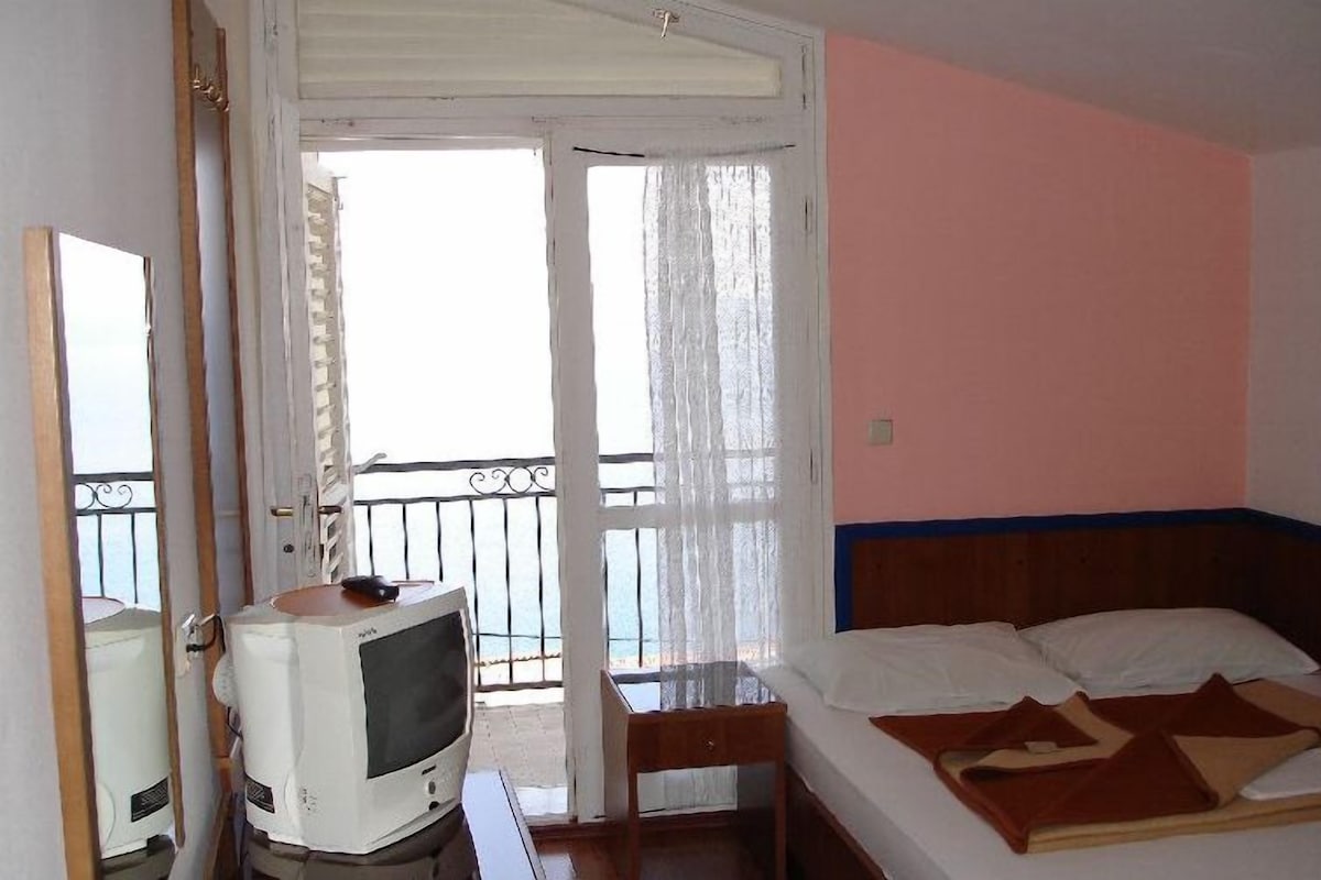 Habitación de hotel con cama, televisión, una silla y un balcón con vistas.