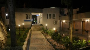 Un camino que lleva a un edificio con recepción, rodeado de árboles e iluminado por farolas.