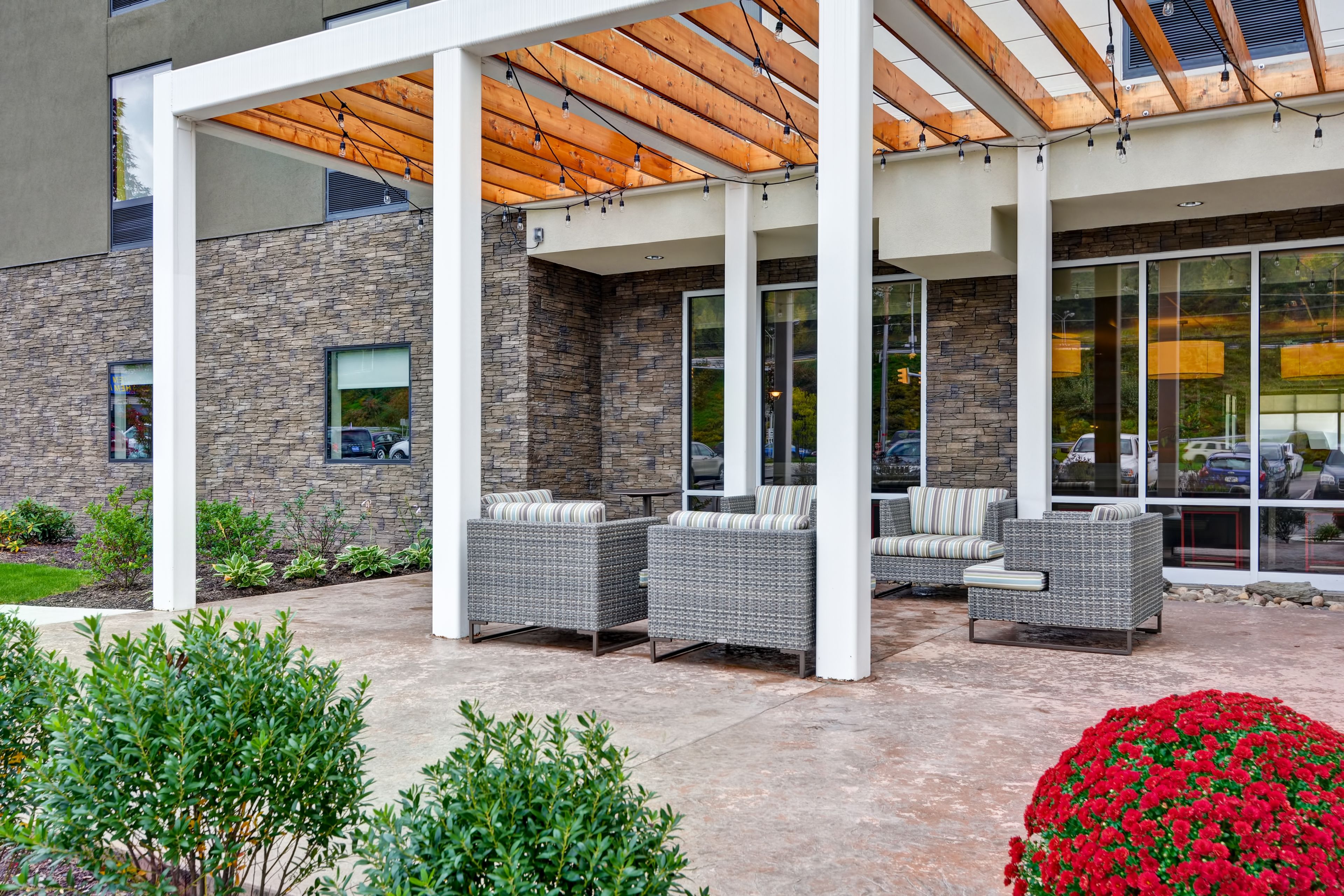 A covered outdoor seating area with wicker furniture and a stone wall backdrop.