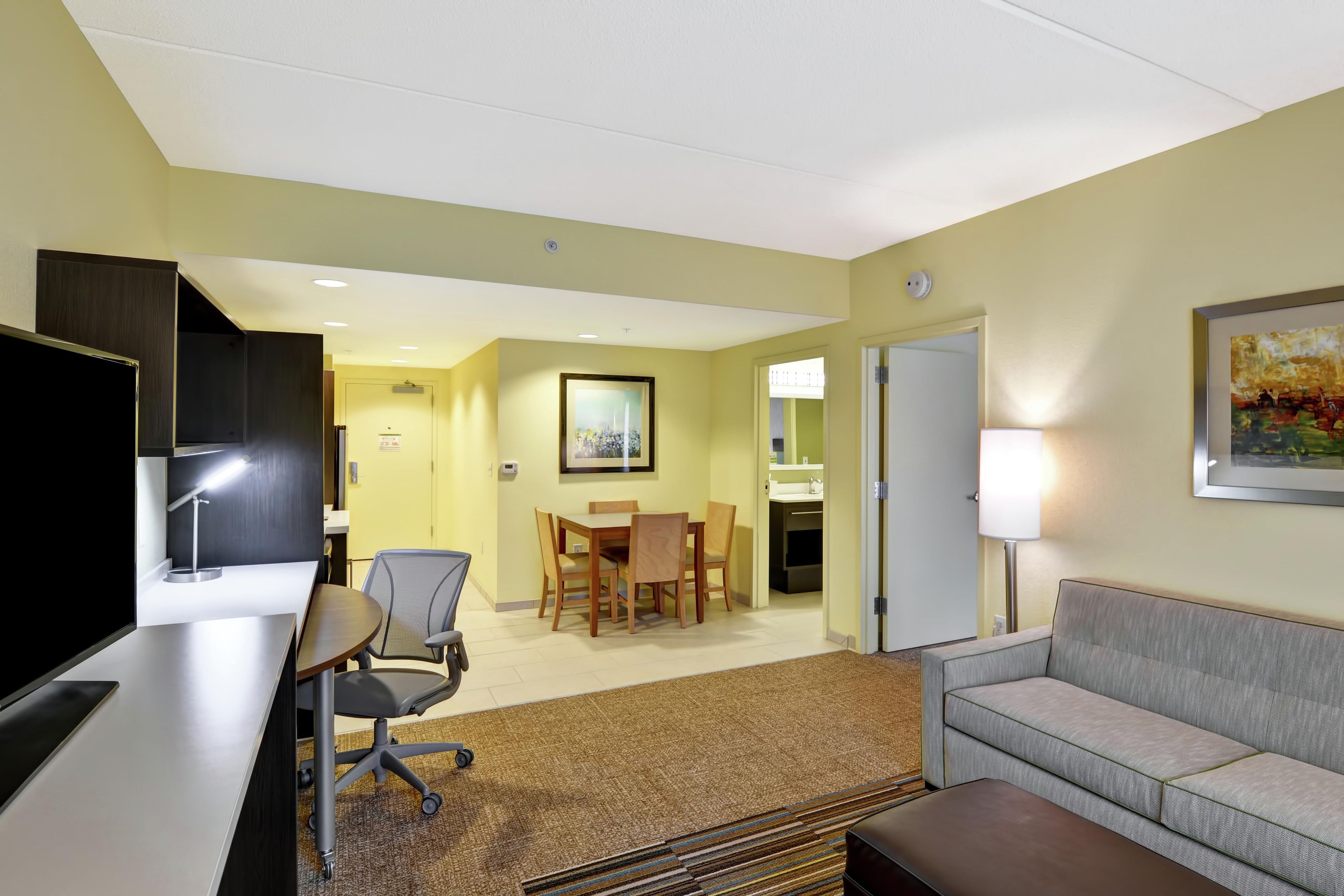 A hotel room with a desk, chair, sofa, and a dining area with a table and chairs.