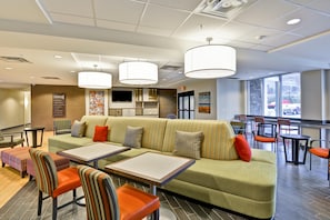 A modern hotel lobby with a green sofa, orange chairs, and a large window.