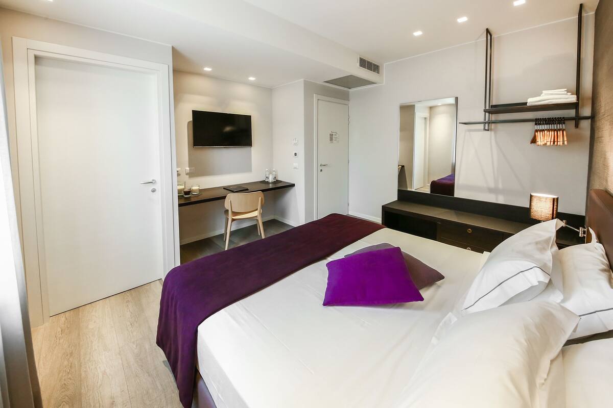 A hotel room with a bed, a desk, a chair, a TV, and a mirror.