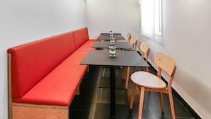 Un espace repas avec un long banc rouge, des chaises en bois et une table sur laquelle sont disposées des bouteilles et des verres.