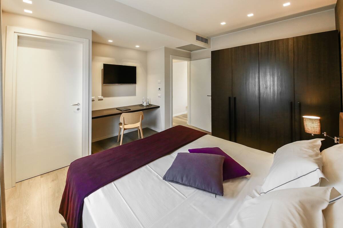 A hotel room with a bed, a desk, a chair, and a wardrobe.