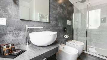 A modern bathroom with a large white sink, a glass-enclosed shower, and a dark tiled wall.