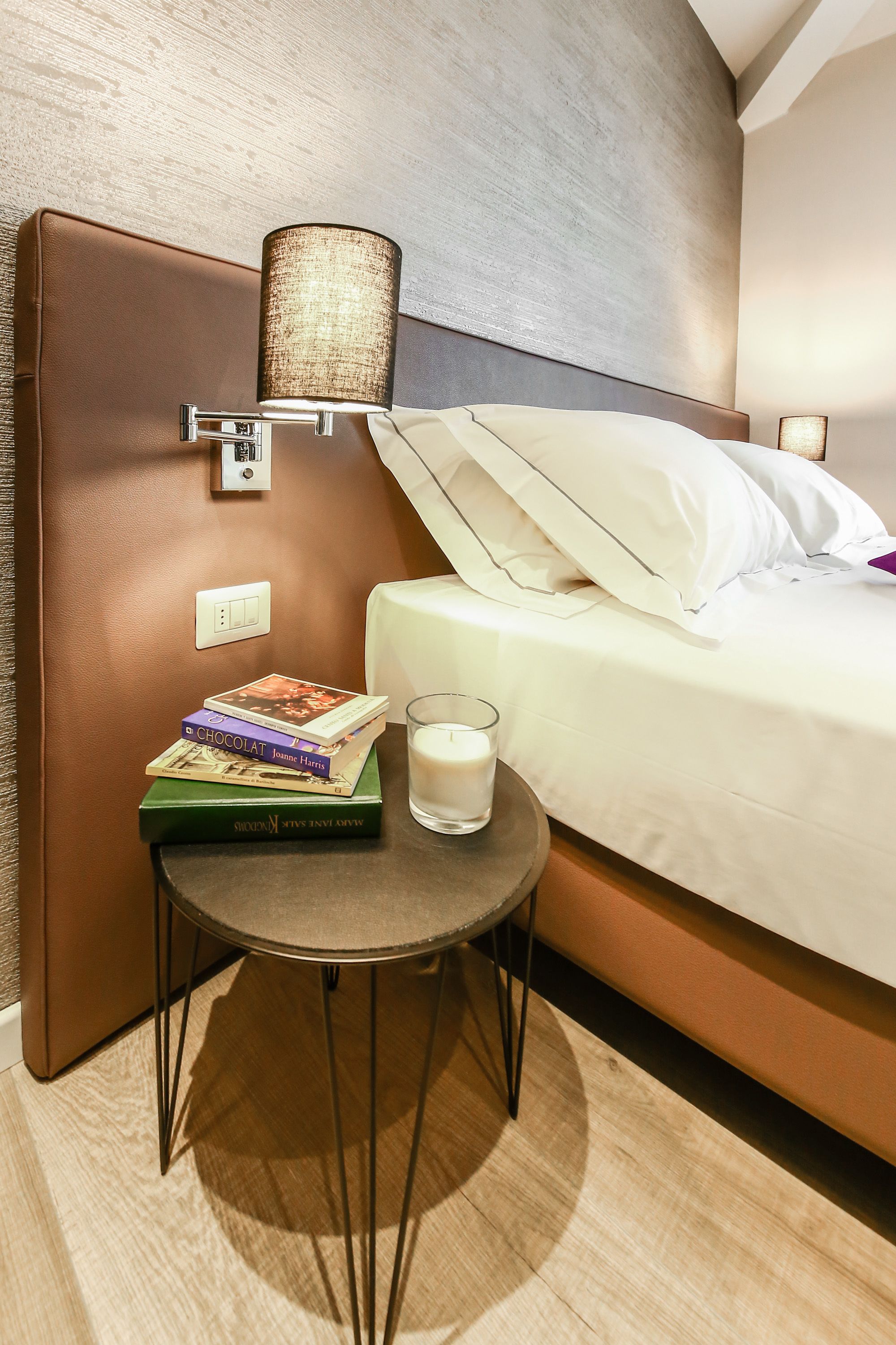 Une chambre d’hôtel avec un lit, une table de chevet avec des livres, un verre de lait et une lampe.