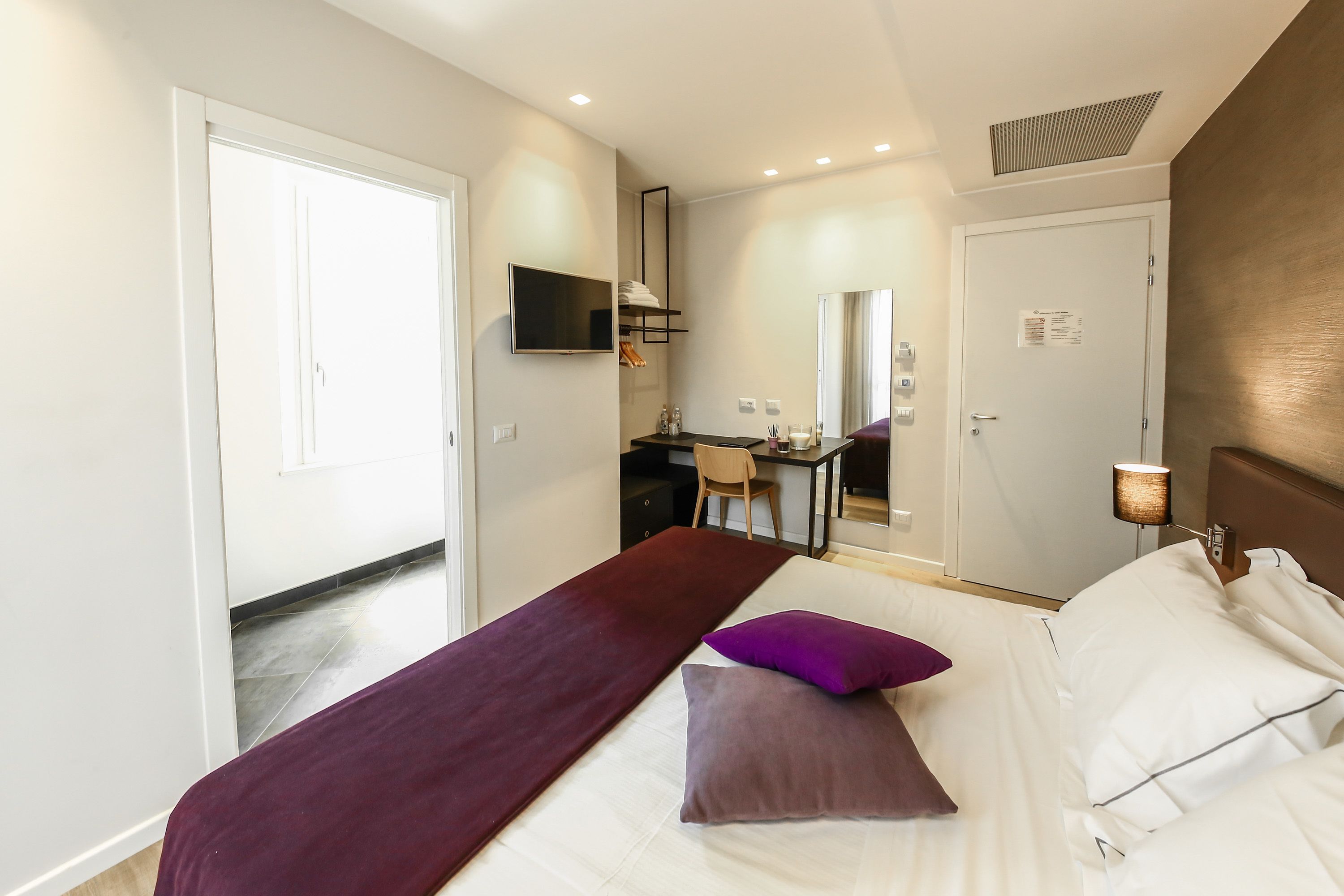 A hotel room with a bed, a desk, a chair, a TV, and a bedside lamp.