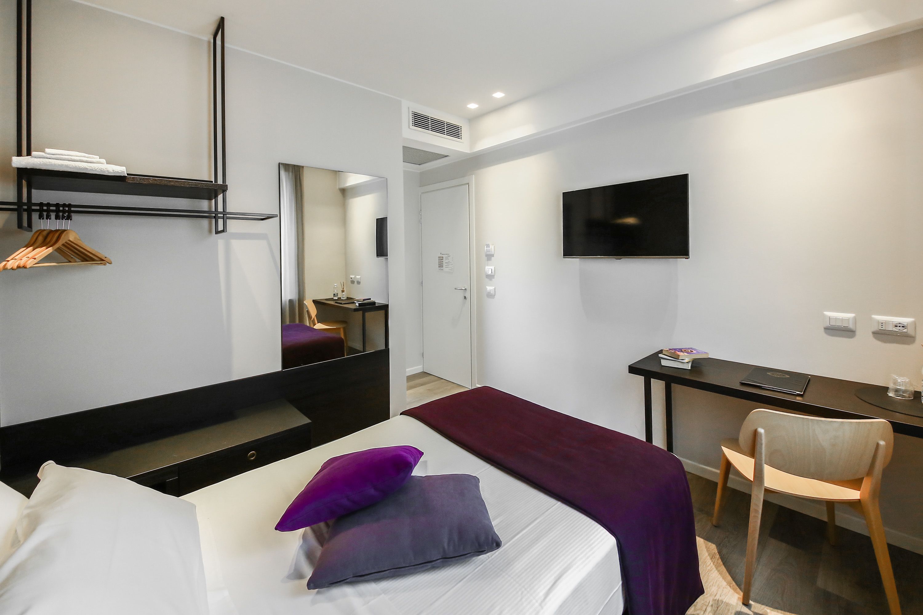 Una habitación de hotel moderna con una cama, un escritorio, una silla, un televisor y un espejo.
