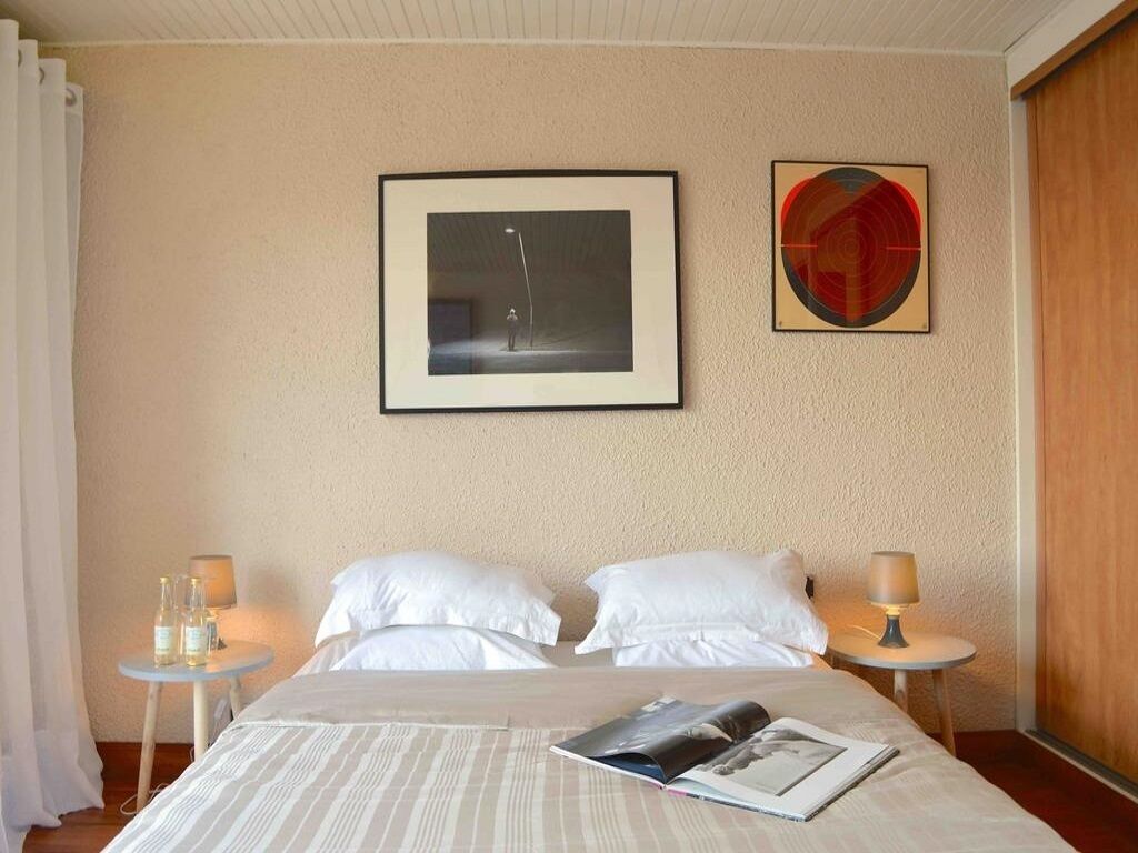 Ein Hotelzimmer mit Bett, zwei Kissen, einem gerahmten Bild, einem Tisch mit Lampe und Wandkunst in Kreisform.